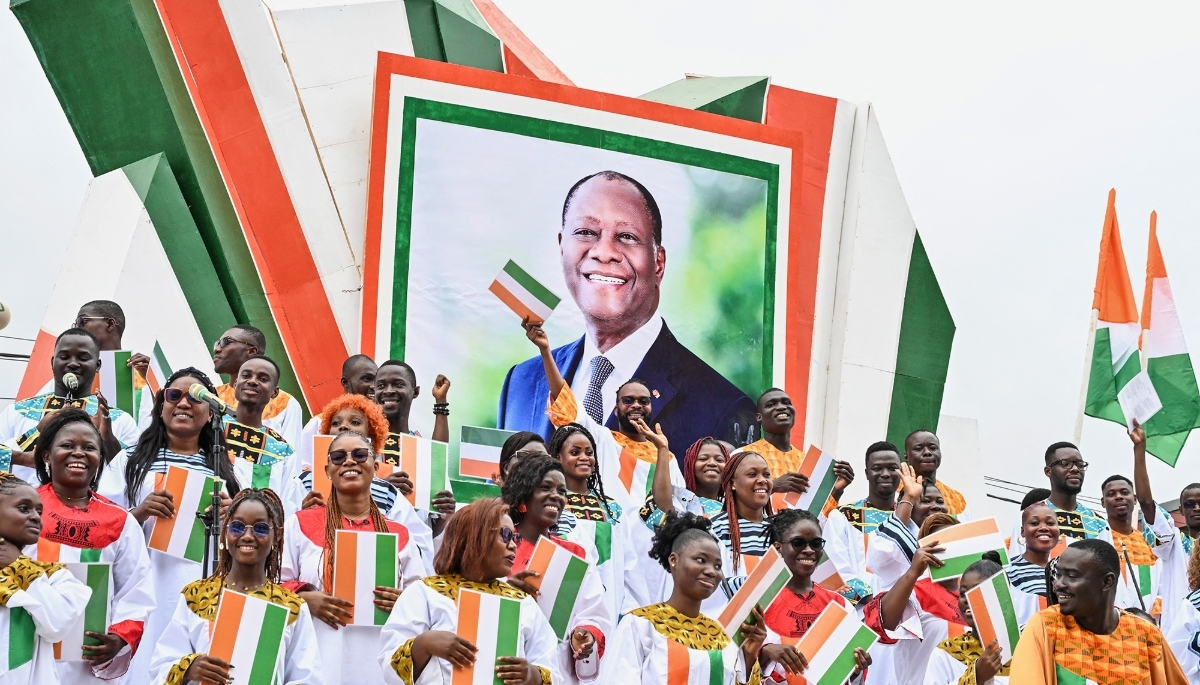 Supporters stand next to a photo of Ivorian President Alassane Ouattara during a military parade marking the 65th anniversary of Ivory Coast's independence in Bouaké on 7 August 2025.