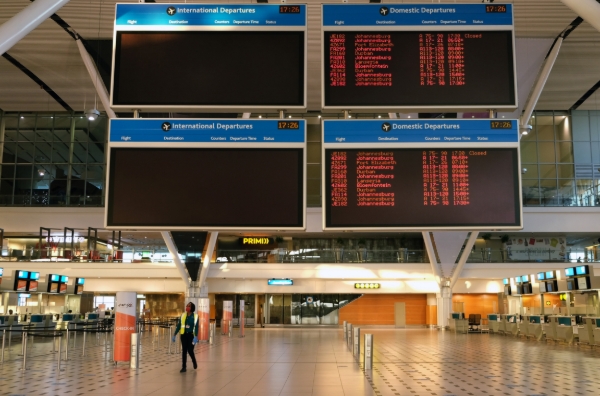 A worker walks beneath electronic flight schedules boards at Cape Town International Airport, run by state-controlled airports company ACSA.